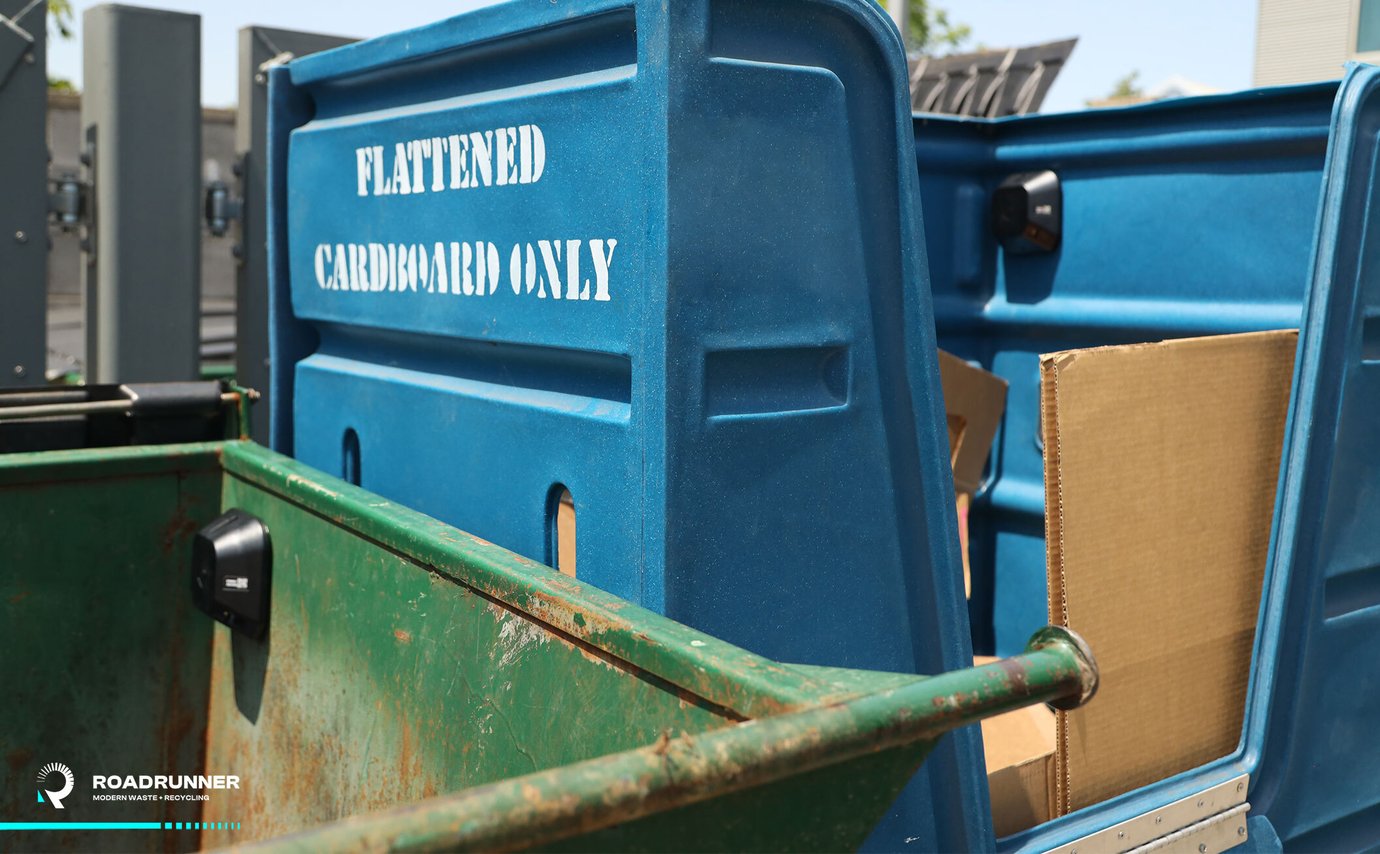 A dumpster next to a cart for flattened cardboard